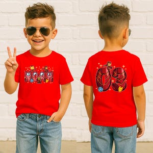 May include: Red t-shirt featuring the word "IRON" with Iron Man graphics and the number "03" on the back. The shirt is worn by a child wearing sunglasses and blue jeans.