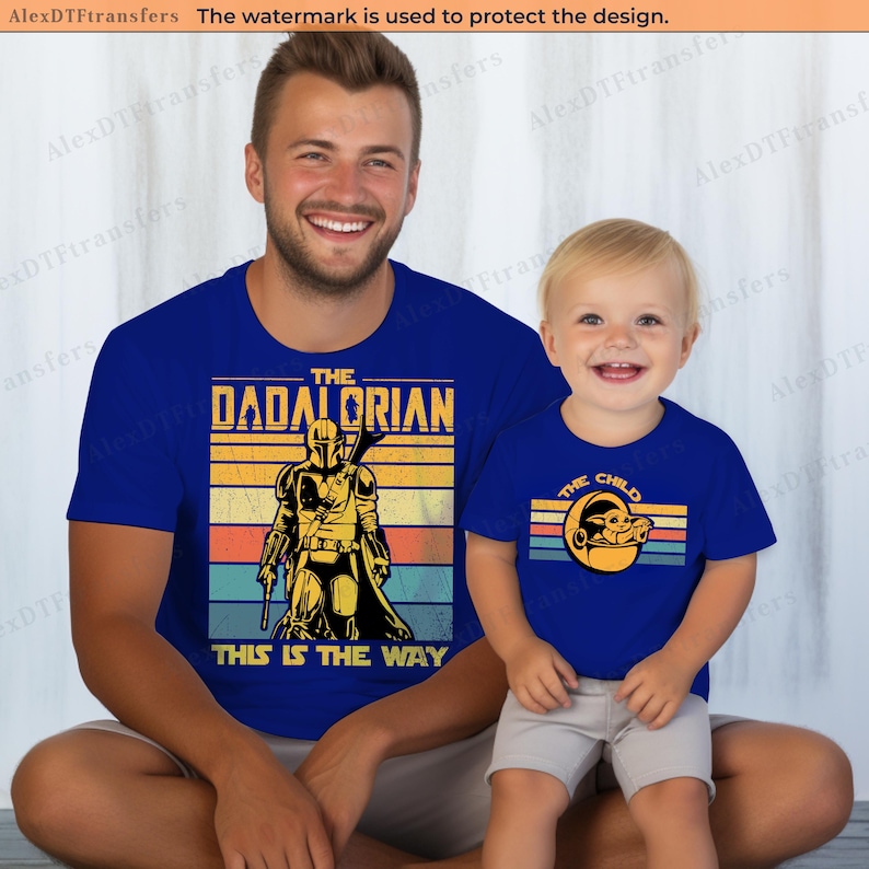 K&ouml;nnte beinhalten: Passende blaue T-Shirts mit Retro-Design. Eines zeigt "The Dadalorian" mit einer Mandalorianer-Grafik, das andere "The Child" mit einer Grogu-Grafik. Beide Shirts haben einen Vintage-Look.