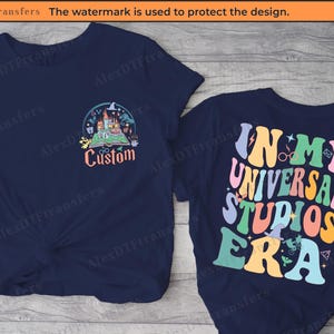 Könnte beinhalten: Zwei marineblaue T-Shirts mit einem grafischen Design. Die Vorderseite eines Shirts zeigt eine Cartoon-Illustration von Hogwarts Castle mit dem Text "Custom". Die Rückseite des anderen Shirts zeigt den Text "In My Universal Studios Era" in einer bunten Retro-Schrift.