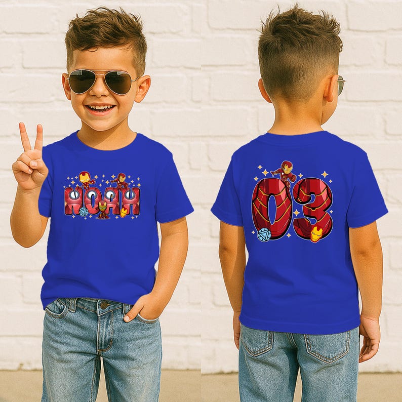 May include: A blue t-shirt featuring the name "NOAH" in a red and gold Iron Man design on the front. The back of the shirt displays the number "03" with Iron Man graphics. The shirt is worn by a child.