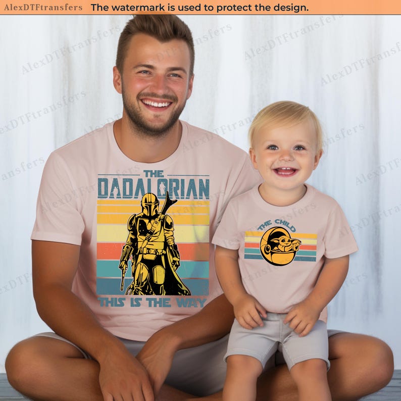 K&ouml;nnte beinhalten: Passende hellrosa T-Shirts mit grafischen Designs. Ein Shirt sagt "The Dadalorian" mit einer Mandalorianer-Illustration und "This is the Way". Das andere Shirt sagt "The Child" mit einer Grogu-Grafik.
