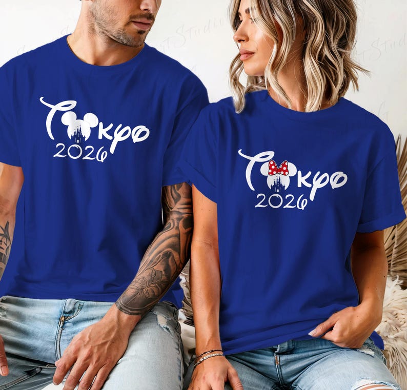 Puede incluir: Dos camisetas azul real con texto blanco "Tokyo 2026" y un dise&ntilde;o inspirado en Mickey Mouse. Una camiseta tiene un lazo de Minnie Mouse. Las camisetas son de manga corta.