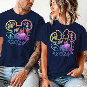 May include: Navy blue t-shirts featuring a colorful Disney design. The design includes a Mickey Mouse head outline with fireworks, a castle, and the text "Disney 2020". One shirt has a Mickey Mouse head, and the other has a Minnie Mouse head.