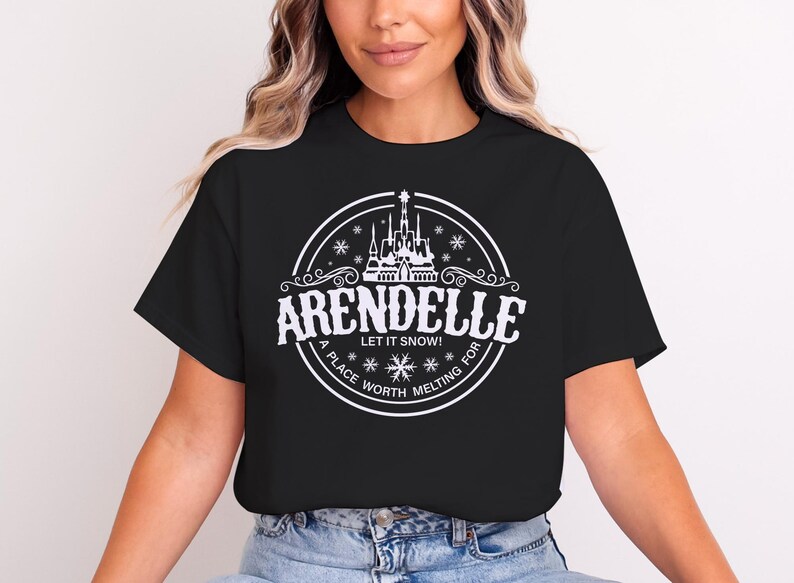 Op de afbeelding: Zwart T-shirt met een witte cirkelvormige afbeelding met het woord "Arendelle" en een kasteelillustratie. De tekst "Let it snow!" en "A place worth melting for" zijn ook inbegrepen.