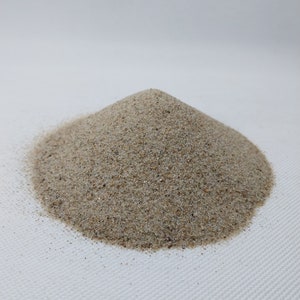 Könnte beinhalten: Ein Haufen hellbraunen Sandes auf einer weißen Oberfläche.