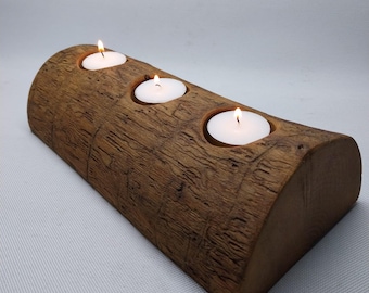 May include: A rustic, wooden candle holder with three lit tea light candles. The holder is made from a section of a log, with a natural, textured finish. The candles are white, and the flames are bright.
