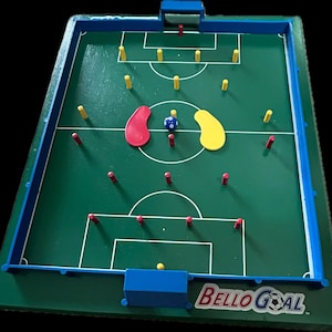 May include: A green tabletop soccer game with a blue frame and a red and yellow player on each side. The game is called "Bello Goal".