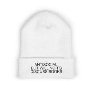 May include: A white beanie with the text "ANTISOCIAL BUT WILLING TO DISCUSS BOOKS" in black. The beanie is made of a soft, knitted material and has a folded brim. This hat is a great accessory for book lovers.