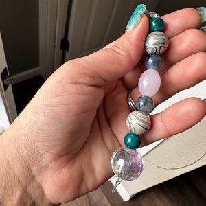 May include: A beaded necklace with a crystal charm, featuring green, pink, and gray beads with marbled patterns.