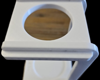 May include: White plastic stand with a circular opening at the top and a flat base. The stand is designed to hold a round object, such as a cup or a jar.