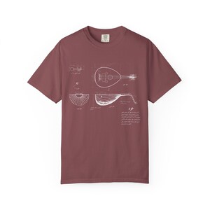 May include: A maroon short-sleeve t-shirt featuring a white technical line drawing of an oud musical instrument. The graphic includes multiple views of the instrument, structural diagrams, and descriptive text in Arabic script centered on the chest.