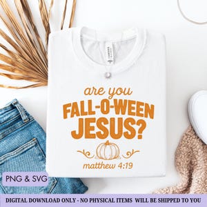 May include: White t-shirt with the text "are you FALL-O-WEEN JESUS?" in orange, along with a pumpkin graphic and the Bible verse Matthew 4:19. The shirt is folded and displayed with jeans and a sweater.