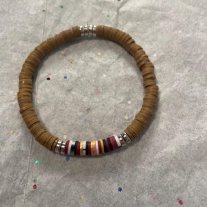 May include: A brown disc bead bracelet with silver accents. The bracelet features a section of colorful beads in red, black, white, and gold. The bracelet is a stylish accessory.