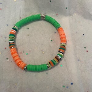 May include: A green and orange beaded bracelet with a silver clasp. The beads are round and have a matte finish.