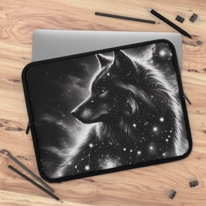 May include: Black laptop sleeve featuring a detailed illustration of a wolf's head with a starry night sky design. The artwork is in shades of black and white, with a zipper closure. The sleeve is designed to protect a laptop.