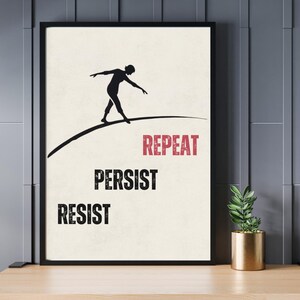 Puede incluir: Impresión artística enmarcada con una silueta negra de una persona equilibrándose sobre una línea curva. Las palabras "REPEAT", "PERSIST" y "RESIST" están impresas en negrita. La obra de arte se muestra sobre una superficie de madera.