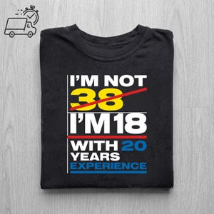 May include: Black t-shirt with the text "I'M NOT 38 I'M 18 WITH 20 YEARS EXPERIENCE" in white, yellow, and blue. The number 38 is crossed out with a red line. The shirt is folded.