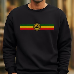 Peut inclure: Sweat-shirt noir avec une bande horizontale aux couleurs du drapeau éthiopien : vert, jaune et rouge. La bande comprend un emblème doré avec un lion au centre.