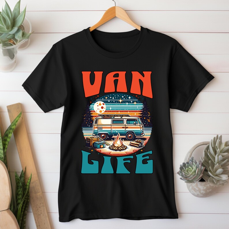 May include: Black t-shirt with a retro design featuring a blue and white van, campfire, and the words "VAN LIFE" in orange and teal. The design includes a full moon and a starry night sky, evoking a camping theme.