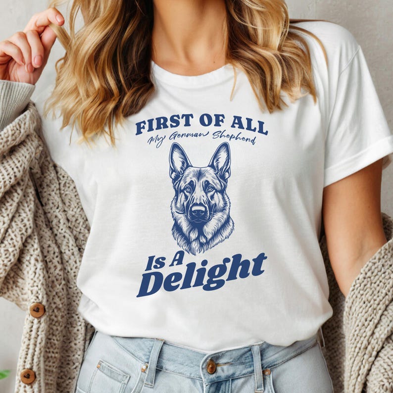 Pu&ograve; includere: Maglietta bianca con una grafica blu di un pastore tedesco. Il testo "FIRST OF ALL My German Shepherd Is A Delight" &egrave; stampato sulla maglietta.