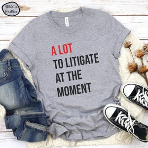 May include: A grey t-shirt with the text "A LOT TO LITIGATE AT THE MOMENT" printed in black and red.