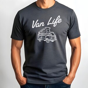 May include: Dark gray t-shirt with the white text "Van Life" above a white illustration of a camper van. The van has an open top and is detailed with windows and wheels. The shirt is short-sleeved.