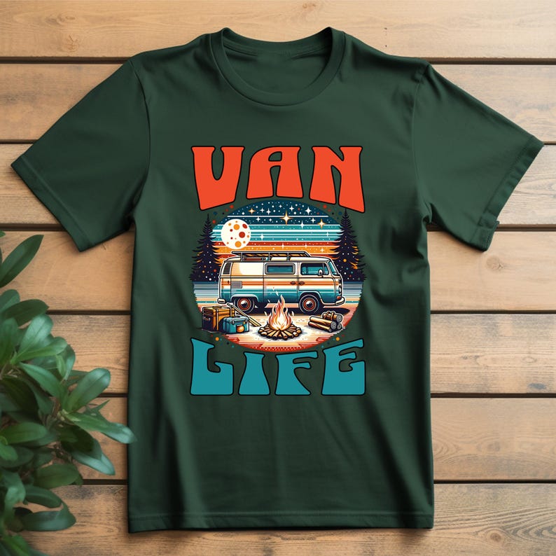 May include: Dark green t-shirt with a retro graphic. The graphic features a vintage van, campfire, and the words "VAN LIFE" in orange and blue. The design evokes a sense of adventure and outdoor living.