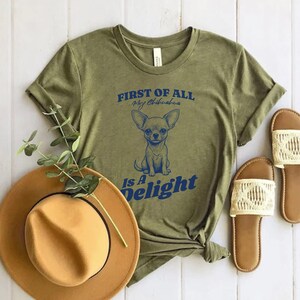 May include: A green t-shirt with the text "FIRST OF ALL My Chihuahua Is A Delight" in blue lettering. A cartoon chihuahua is pictured in the center of the shirt.