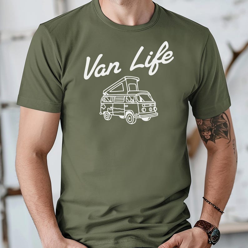May include: Olive green t-shirt with the white text "Van Life" above a white line drawing of a camper van. The camper van has a pop-up roof and is facing forward.