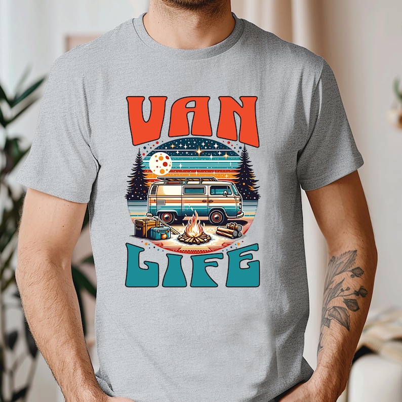 May include: A gray t-shirt featuring a retro design with the words "VAN LIFE" in orange and teal. The graphic includes a vintage van, campfire, and trees, evoking a camping theme. The design is set against a sunset backdrop.