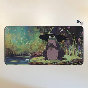May include: A green frog wearing a black witch hat sits on a rock by a pond. The frog is holding a small bunch of flowers in its hands. The background is a lush green forest with a pond and lily pads.