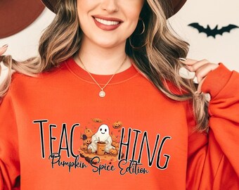 Op de afbeelding: Oranje sweatshirt met de tekst "TEACHING Pumpkin Spice Edition" en een cartoon-spook dat een pompoen vasthoudt.