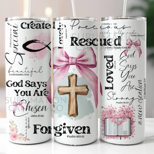 May include: A white tumbler with a pink watercolour design featuring a cross, a bow, and a fish. The tumbler has inspirational text with bible verses, including "Created", "Loved", "Rescued", "Forgiven", "God Says You Are Chosen", "God Says You Are Strong", and "A New Creation".