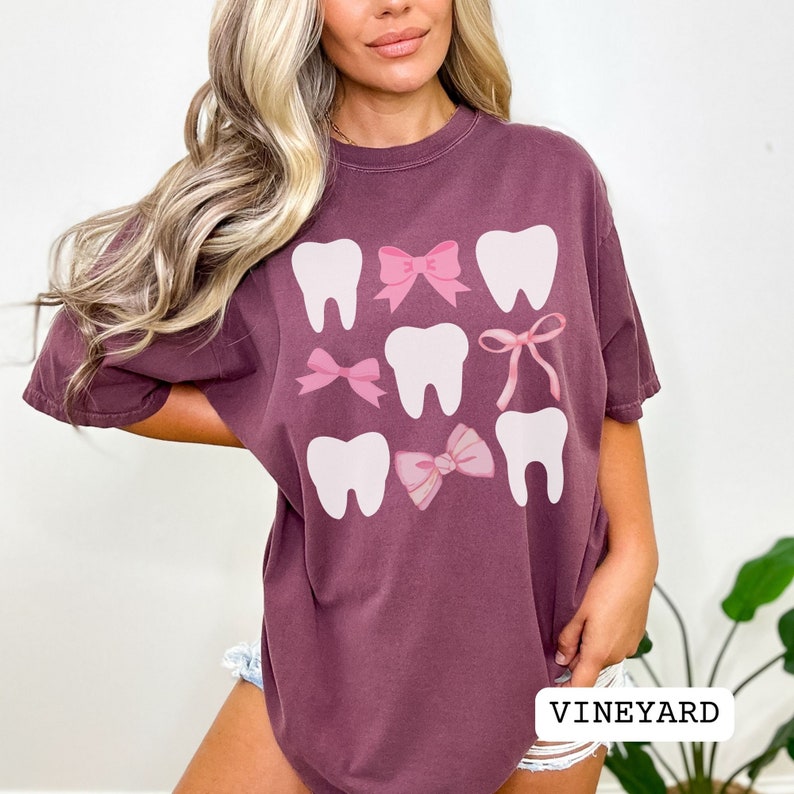 May include: A maroon oversized t-shirt with a graphic design of white teeth and pink bows. The text "VINEYARD" is visible at the bottom of the image.