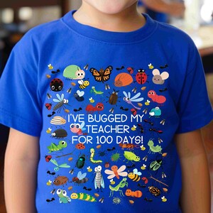 May include: Royal blue t-shirt featuring a colorful array of cartoon insects, including ladybugs, bees, and butterflies. The text "I'VE BUGGED MY TEACHER FOR 100 DAYS!" is printed in white. A fun and educational design for kids.