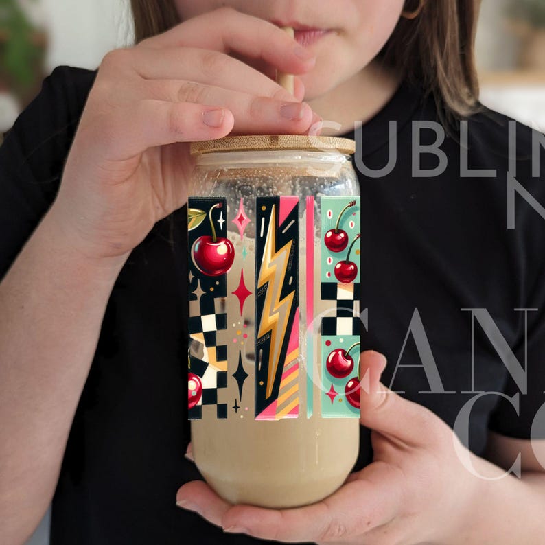 May include: A clear glass tumbler with a black, white, and yellow geometric design featuring cherries and lightning bolts. The tumbler has a bamboo lid and a straw.