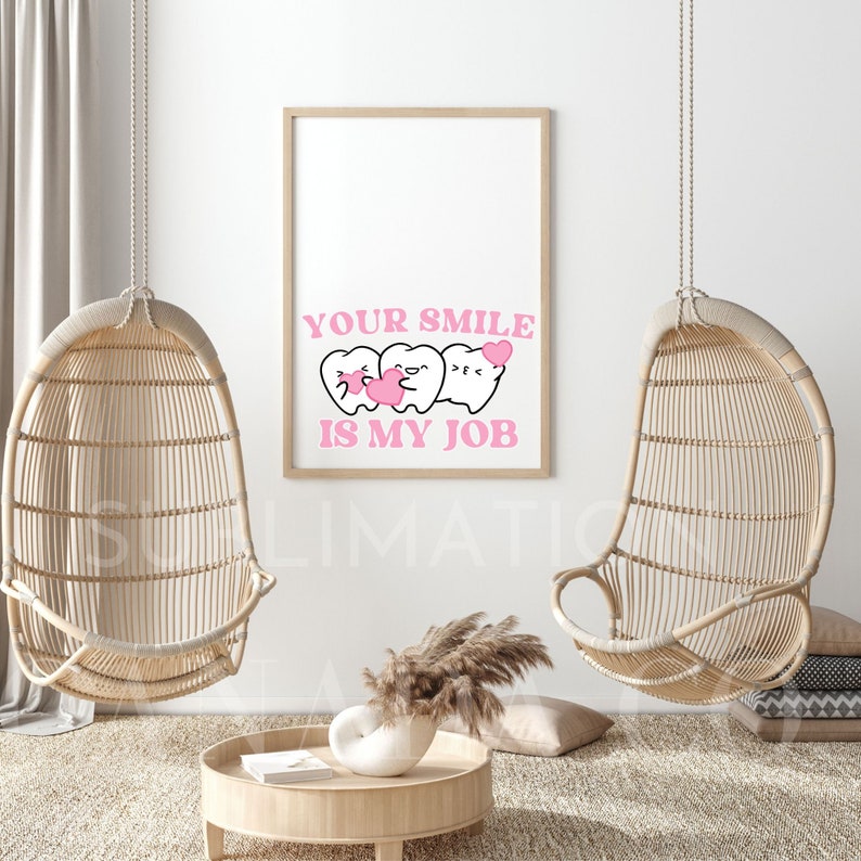May include: A white framed print with a pink background and the text "YOUR SMILE IS MY JOB". Three cartoon teeth with pink hearts are shown above the text. The print is hanging on a white wall with two wicker hanging chairs on either side.