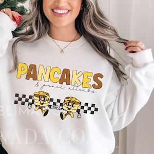 May include: White sweatshirt with a graphic design of two cartoon pancakes with faces and the text "PANCAKES & panic attacks".