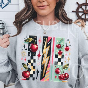 May include: A gray sweatshirt with a colorful graphic design featuring cherries, lightning bolts, and checkered patterns. The design is in a retro style.