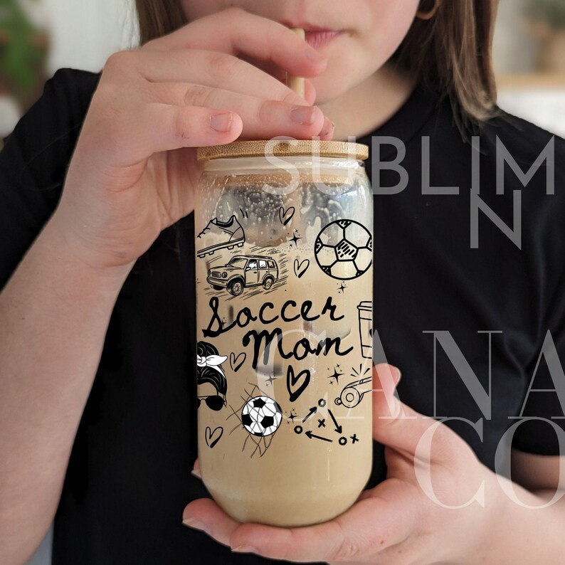 May include: A clear glass tumbler with a bamboo lid and a straw. The tumbler has a black and white design with the words "Soccer Mom" and soccer-related imagery.