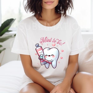 May include: White t-shirt with a pink cartoon tooth and a tube of toothpaste. The text "Mint to be!" is printed on the shirt.