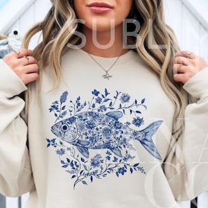 May include: A cream-colored sweatshirt with a blue and white floral design of a fish. The fish is surrounded by blue and white flowers and leaves.