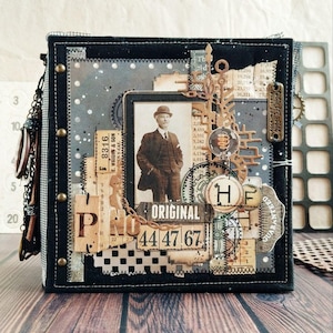 Könnte beinhalten: Ein handgefertigtes, quadratisches Scrapbook-Album mit einem schwarzen Stoffeinband. Die Vorderseite zeigt ein Vintage-Foto eines Mannes, dekorative Papierschnipsel, Metallverzierungen und das Wort "ORIGINAL". Das Album ist mit Ketten und Nieten verziert.