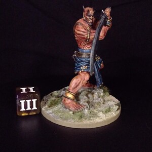 May include: A hand-painted miniature figure of a horned demon wielding a curved sword. The figure is reddish-brown with blue accents and gold jewelry, standing on a rocky base. A die showing the number three is next to the figure.