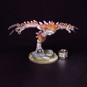 May include: A detailed miniature figurine of a creature with orange and purple accents, sharp claws, and spiky protrusions. The figure is posed dynamically on a rocky base, with a die showing the number three.