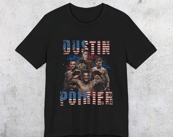 May include: Black t-shirt with a graphic of a group of men in a boxing ring. The graphic is set against an American flag background. The text "Dustin Poirier" is printed on the shirt.
