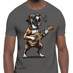 May include: Dark gray t-shirt featuring a cartoon Boxer dog playing a ukulele and singing. The dog is brown and white, wearing sunglasses and a blue collar. Musical notes float above the dog. The shirt is a short-sleeve style.