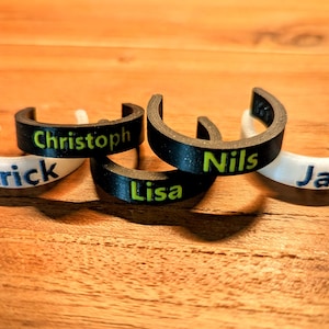 Peut inclure: Cinq étiquettes de nom personnalisées, deux blanches et trois noires, avec les noms Patrick, Christoph, Lisa, Nils et Jan imprimés en vert.