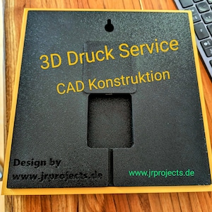 Könnte beinhalten: Ein schwarzes quadratisches Schild mit gelbem Rand, das 3D-Druck- und CAD-Konstruktionsdienste bewirbt. Das Schild trägt die Aufschrift "3D Druck Service CAD Konstruktion" und enthält die Website "www.jrprojects.de".
