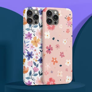 May include: Two phone cases with floral patterns. One is white with purple, orange, and yellow flowers. The other is pink with pink, white, and orange flowers. The cases are displayed on a blue surface.